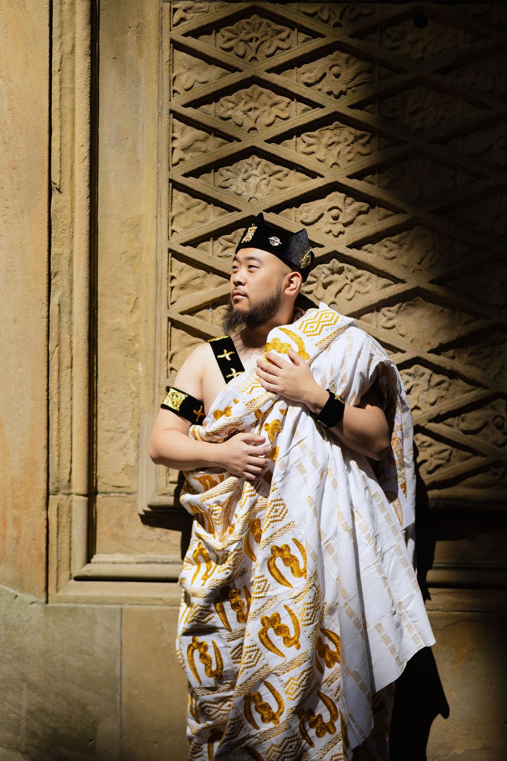 JiaJie in a white and gold wrap, standing beside a stone column.